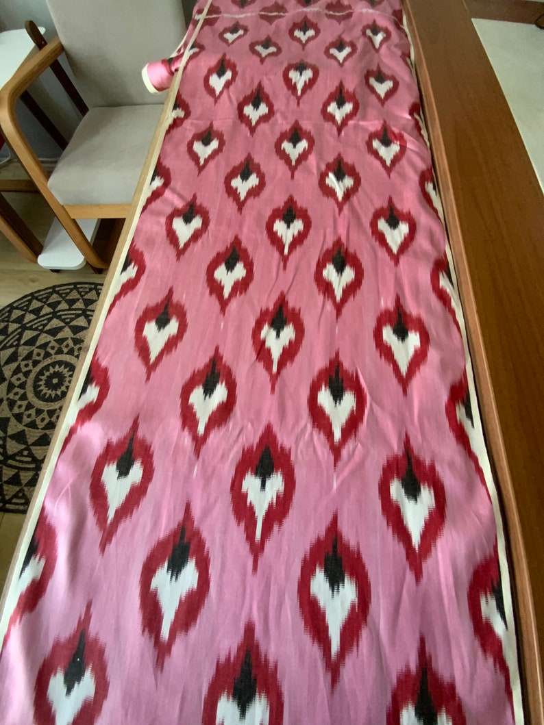 May include: Pink fabric with a repeating pattern of white, red, and black teardrop shapes.