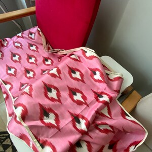 May include: Pink fabric with a white and black ikat pattern. The fabric is folded and draped over a chair.