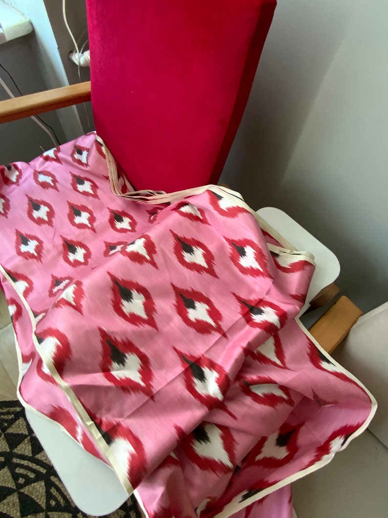 May include: Pink fabric with a white and black ikat pattern. The fabric is folded and draped over a chair.