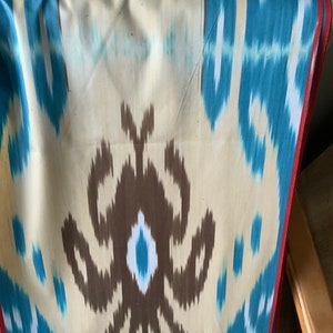 May include: A close-up of a fabric with a brown, blue, and white ikat pattern. The fabric has a red border.