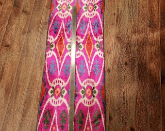 May include: A pink, white, orange, blue, and green ikat fabric with a repeating pattern. The fabric is approximately 45 inches long.