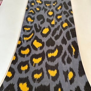Könnte beinhalten: Ein grauer Stoff mit einem schwarzen und gelben Leopardenmuster. Der Stoff hat einen dezenten Glanz und eine weiche Textur.