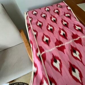 May include: Pink fabric with a white and black ikat pattern. The fabric has a white and black trim along the edges.