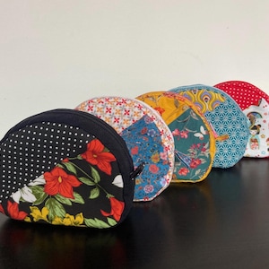 Peut inclure: Une rangée de cinq pochettes zippées en demi-cercle avec différents motifs de tissu. Les motifs incluent des pois, des imprimés floraux et des motifs géométriques. Chaque pochette a une fermeture éclair noire et une petite boucle sur le côté.