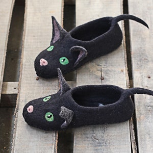 May include: A pair of black felt slippers shaped like cats with green eyes and pink noses.