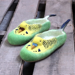 Op de afbeelding: Een paar groene wollen pantoffels met een geel en zwart vogelontwerp. De pantoffels hebben een lange staart en een vogelkop met een gele snavel.