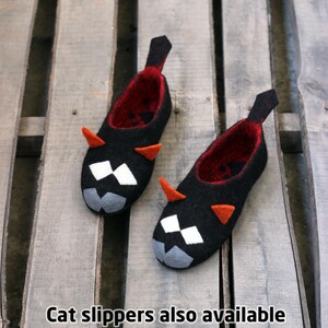 Peut inclure: Une paire de chaussons noirs en forme de chat avec des int&eacute;rieurs rouges, des cornes oranges et des d&eacute;tails faciaux blancs et gris. Les chaussons ont une languette noire au talon. Texte: "Cat slippers also available see link in description".