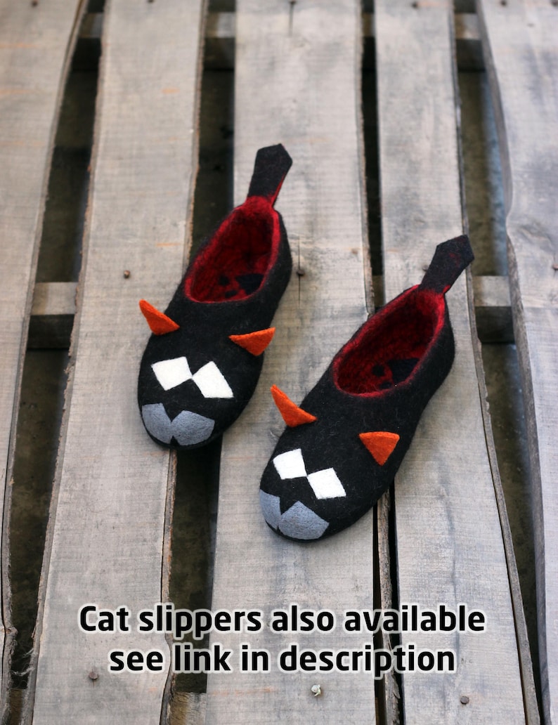 Peut inclure: Une paire de chaussons noirs en forme de chat avec des int&eacute;rieurs rouges, des cornes oranges et des d&eacute;tails faciaux blancs et gris. Les chaussons ont une languette noire au talon. Texte: "Cat slippers also available see link in description".