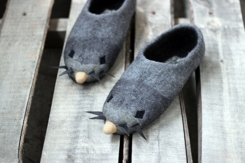 Peut inclure: Une paire de pantoufles en feutre gris au design fantaisiste. Chaque pantoufle pr&eacute;sente un nez beige clair, des yeux noirs en forme de losange et des pointes noires. Les pantoufles sont con&ccedil;ues pour ressembler &agrave; une taupe.