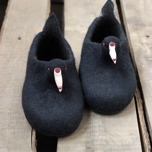 Op de afbeelding: Een paar zwarte wollen pantoffels met een vogelontwerp. De pantoffels hebben een roze snavel en rode ogen.