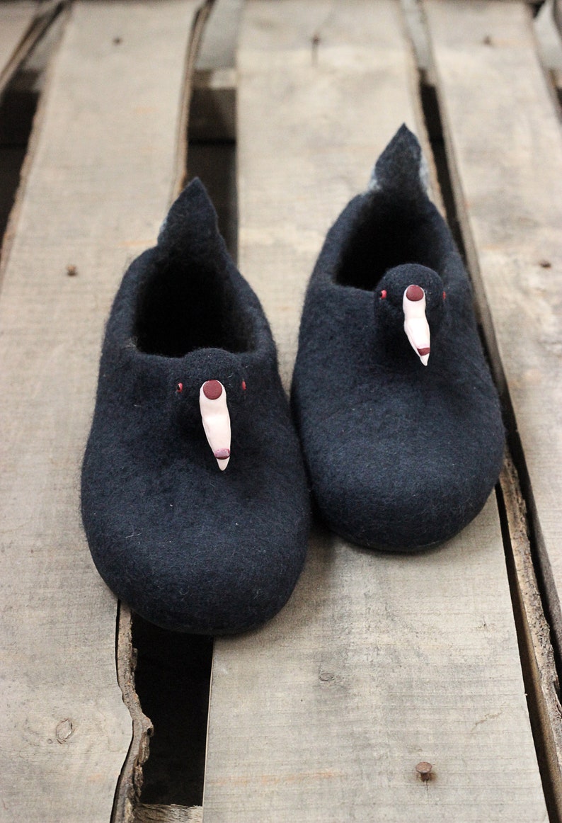 Op de afbeelding: Een paar zwarte wollen pantoffels met een vogelontwerp. De pantoffels hebben een roze snavel en rode ogen.