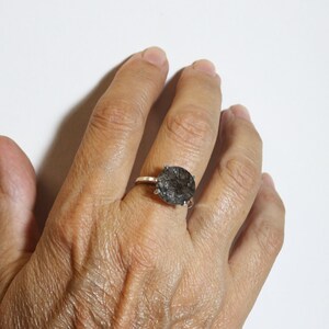 May include: A silver ring with a large oval-shaped black gemstone. The gemstone has a unique, cloudy, and textured appearance.