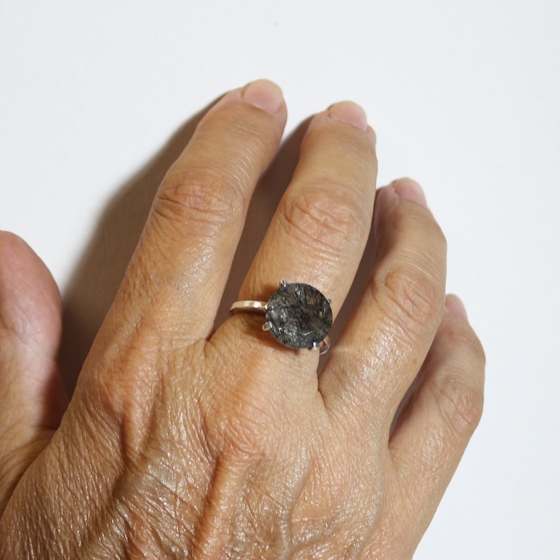May include: A silver ring with a large oval-shaped black gemstone. The gemstone has a unique, cloudy, and textured appearance.
