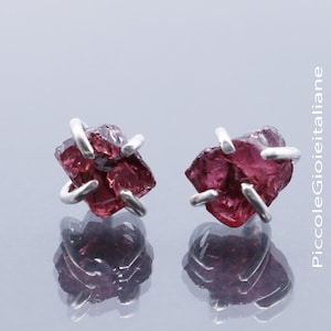 Könnte beinhalten: Ein Paar silberne Ohrstecker mit rohen, roten Granatsteinen. Die Edelsteine sind in einem schlichten, modernen Design gefasst.