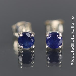 May include: A pair of silver stud earrings with small, round, dark blue sapphire gemstones.