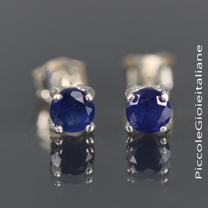May include: A pair of silver stud earrings with small, round, dark blue sapphire gemstones.