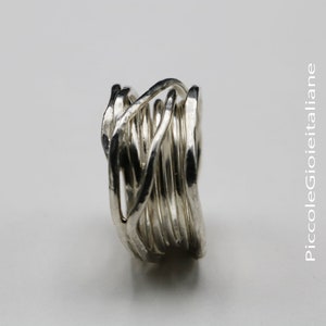 Op de afbeelding: Een zilveren ring met een uniek, geweven ontwerp. De ring heeft meerdere strengen metaal die in elkaar grijpen om een ​​gestructureerd, opvallend stuk te cre&euml;ren. Het ontwerp van de ring is modern en artistiek, geschikt voor dagelijks gebruik of speciale gelegenheden.