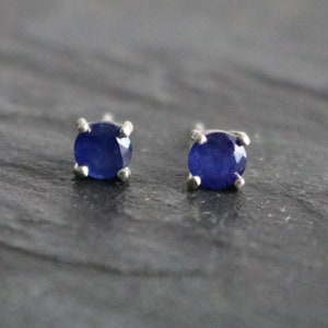 May include: A pair of silver stud earrings with small, round, dark blue sapphire gemstones.