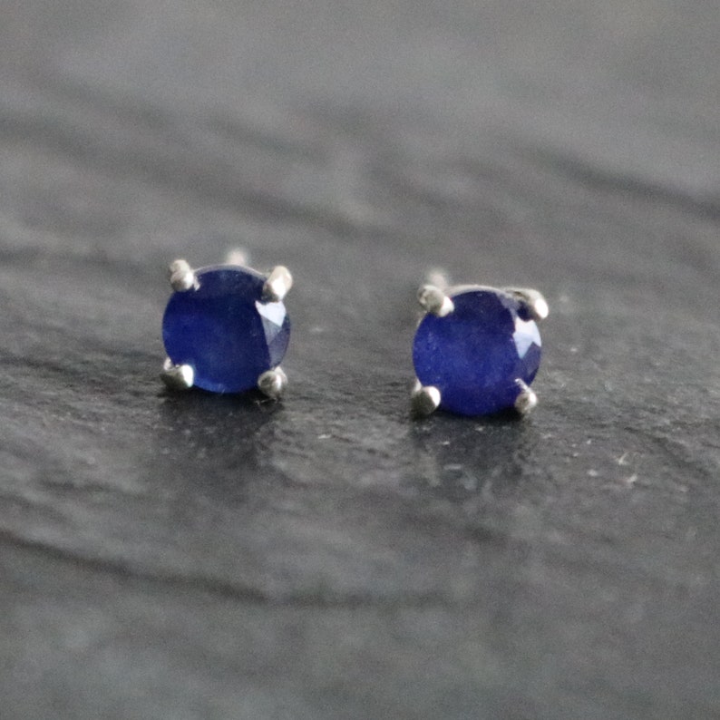 May include: A pair of silver stud earrings with small, round, dark blue sapphire gemstones.