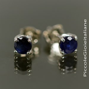May include: A pair of silver stud earrings with round blue sapphire gemstones.