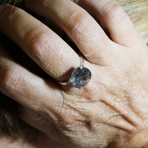 May include: A silver ring with a large, round, clear quartz gemstone with black inclusions. The gemstone is set in a simple, silver band.