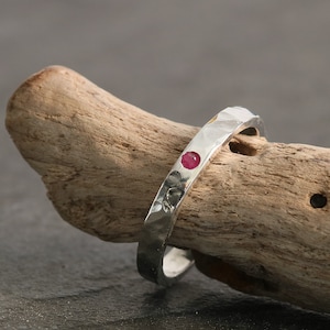 Puede incluir: Un anillo de plata con textura martillada y una sola piedra preciosa roja engastada en la banda.