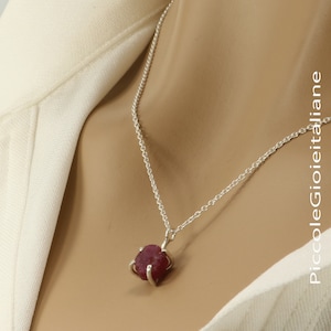 May include: A silver chain necklace with a pendant featuring a large, red, rough-cut ruby stone.
