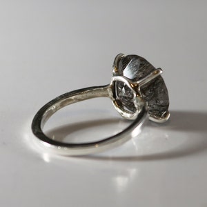 May include: A silver ring with a large, clear, faceted gemstone with black inclusions. The ring is set in a prong setting.