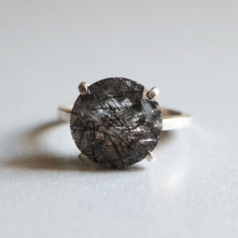 May include: A silver ring with a large, round, clear quartz stone with black inclusions. The stone is set in a four-prong setting.