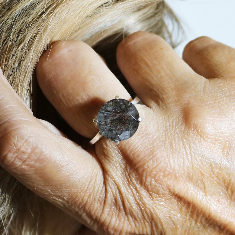 May include: A silver ring with a large, round, dark gray gemstone. The gemstone has a cloudy, translucent appearance.