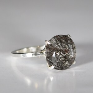 May include: A silver ring with a large, round, clear quartz stone with black and brown inclusions. The stone is set in a simple, silver band.