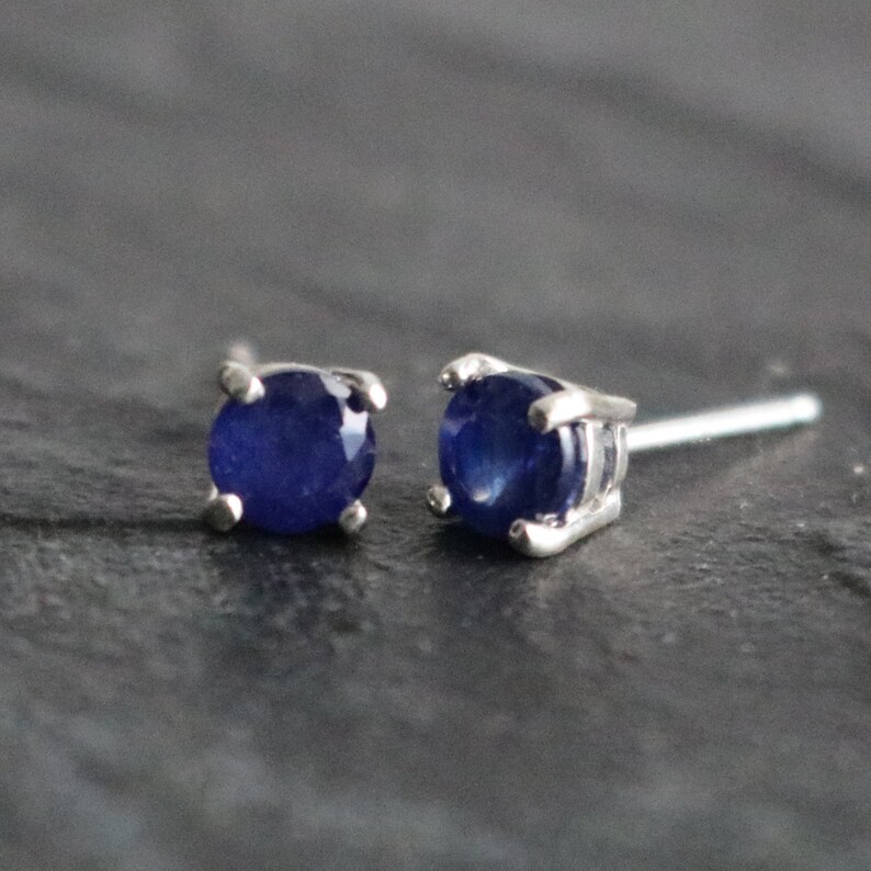 May include: A pair of silver stud earrings with round blue sapphire gemstones.