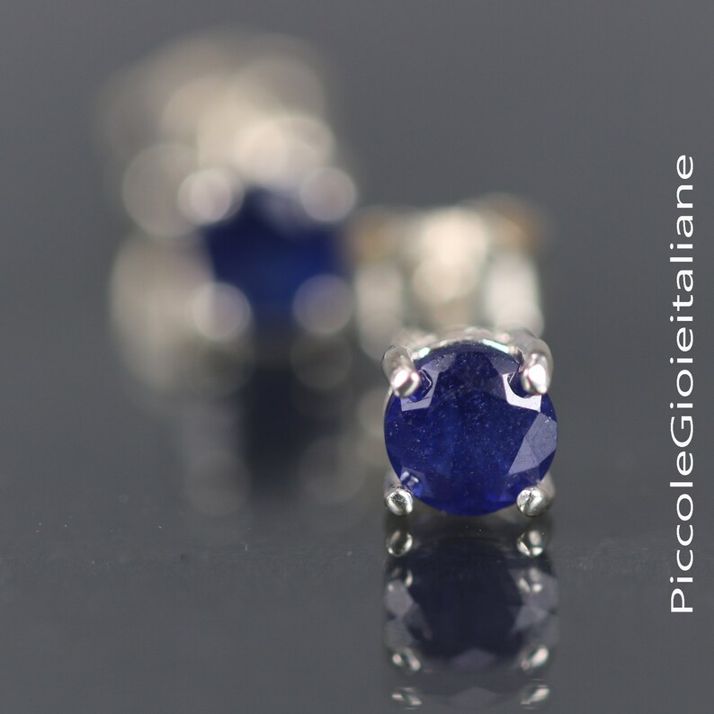 May include: A pair of silver stud earrings with a round, dark blue sapphire gemstone in each earring.