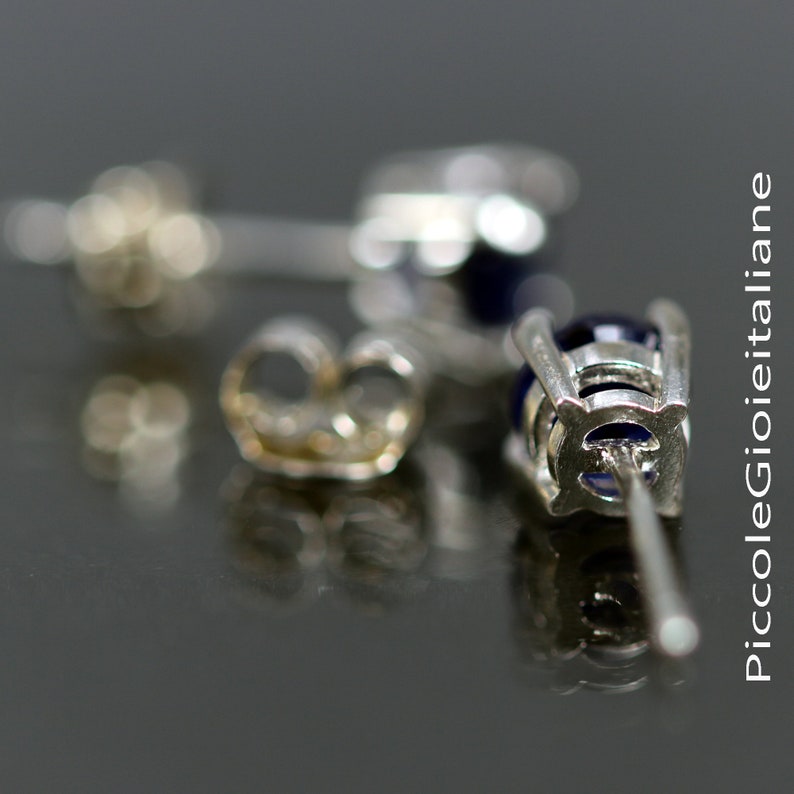 May include: Close-up of a pair of silver earrings with blue gemstones. The earrings have a post back closure and are designed with a delicate, intricate pattern.