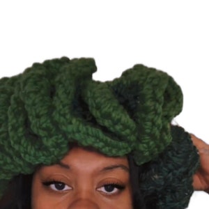 May include: A dark green crocheted headband with a thick, textured design. The headband is worn on a person's head.