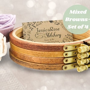 May include: Set of four embroidery hoops in various shades of brown. The hoops are made of wood and have a brass screw closure. The hoops are stacked on top of each other.