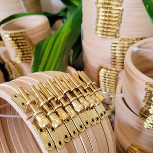 May include: Close-up of a set of wooden embroidery hoops with gold-toned metal tightening screws. The hoops are stacked and the screws are visible on the side.