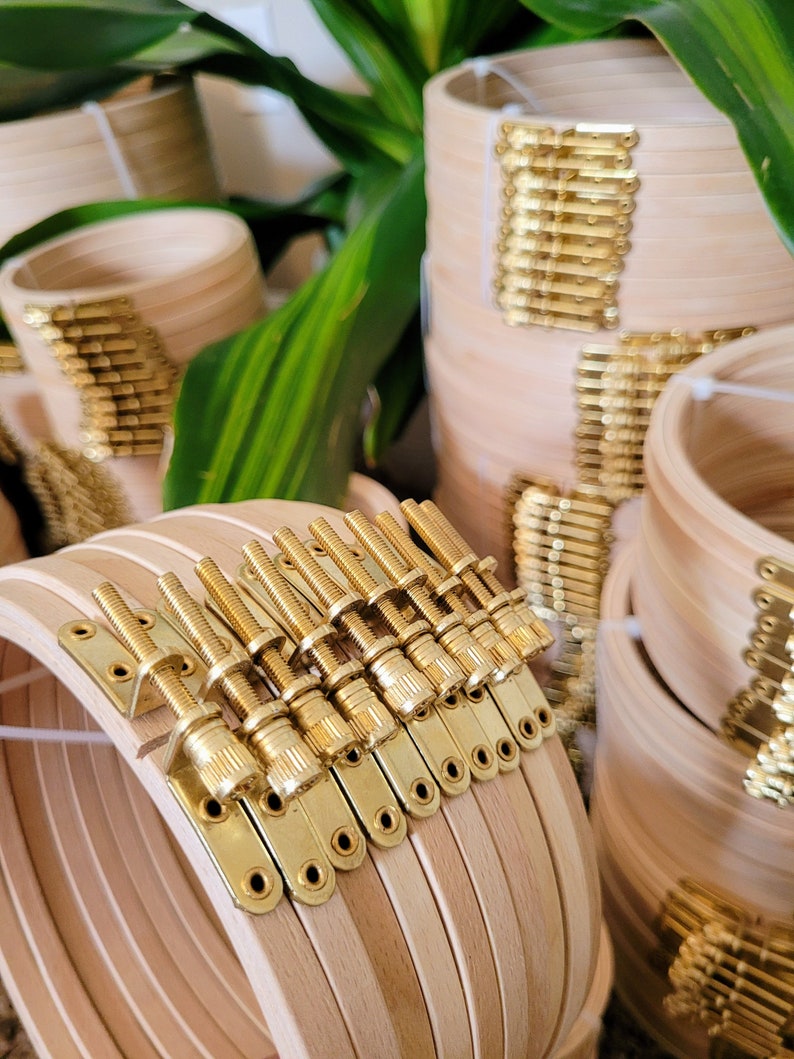 May include: Close-up of a set of wooden embroidery hoops with gold-toned metal tightening screws. The hoops are stacked and the screws are visible on the side.