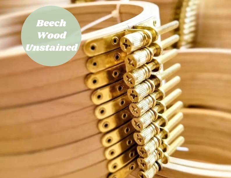 May include: Close-up of a stack of unfinished beech wood embroidery hoops with brass screw-on tightening mechanisms.  "Beech Wood Unstained" is written on a green circle.