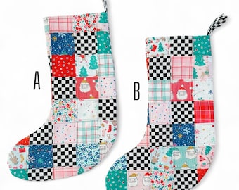 May include: Two Christmas stockings with patchwork designs. Each stocking features a mix of red, green, blue, and white squares with holiday-themed patterns, including Santa Claus, trees, and snowflakes. The tops and hanging loops have a black and white checkered pattern.