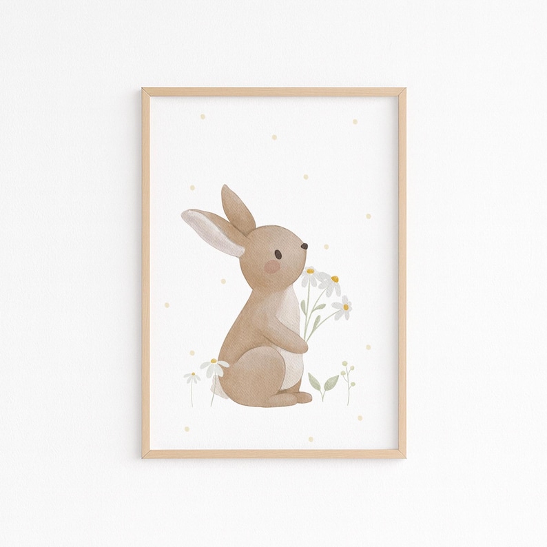 May include: Watercolor illustration of a tan bunny holding white daisies, set against a white background with yellow polka dots. The artwork is framed in a light brown wooden frame, perfect for nursery decor.