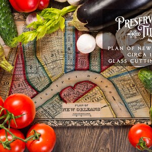 May include: A vintage map of New Orleans, circa 1860, printed on a glass cutting board. The board is surrounded by fresh vegetables, including tomatoes, cucumbers, and eggplant.