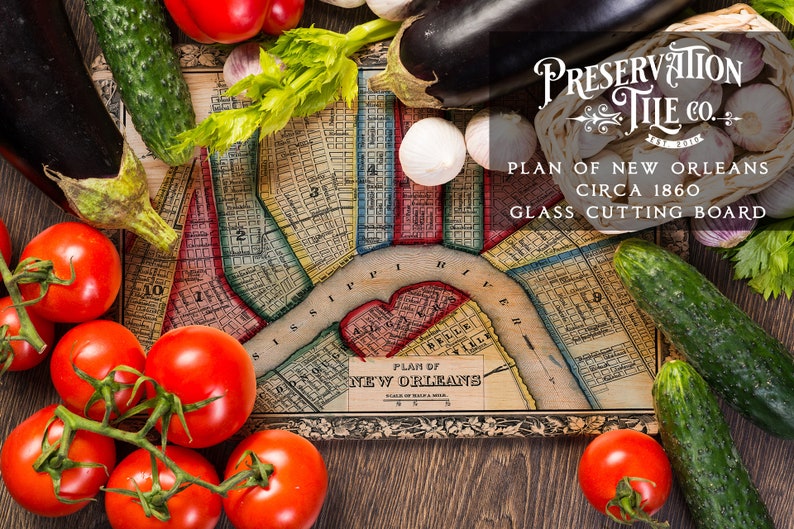 May include: A vintage map of New Orleans, circa 1860, printed on a glass cutting board. The board is surrounded by fresh vegetables, including tomatoes, cucumbers, and eggplant.