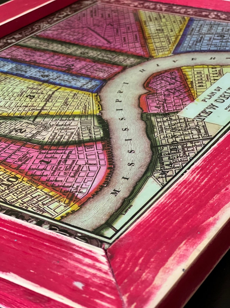 May include: A framed vintage map of New Orleans, Louisiana, with a pink wood frame. The map shows the city's streets and the Mississippi River. The title of the map is "Plan of New Orleans".
