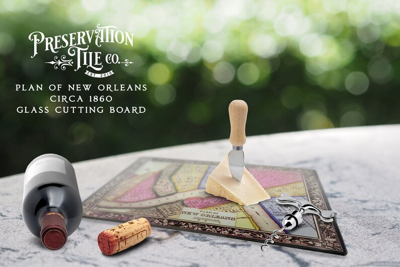 May include: A glass cutting board featuring a vintage map of New Orleans, circa 1860. The board is surrounded by a decorative border and includes the text "Preservation Tile Co.". The image also shows a cheese knife, a corkscrew, and a wine bottle.