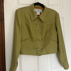 May include: A green linen jacket with a collared neckline and button closure. The jacket has two pockets and long sleeves. The label on the jacket reads "Fashioning Touches".
