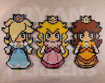May include: Three pixel art figures of Princess Peach, Peach, and Daisy from the Super Mario Bros. video game series. The figures are made of colorful beads and are arranged in a row.