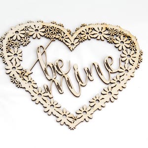 Könnte beinhalten: Ein herzförmiges Schild aus Holz mit einem floralen Design und den Worten "be mine" in einer kursivschrift.