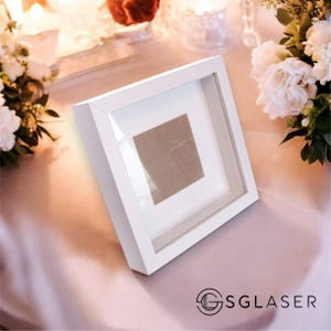 Könnte beinhalten: Weißer Bilderrahmen mit einer klaren Glasscheibe und einem weißen Passepartout. Der Rahmen steht auf einer weißen Tischdecke.