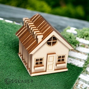 Può includere: Una piccola casa modello in legno con tetto marrone e pareti bianche. La casa ha una finestra, una porta e un camino.